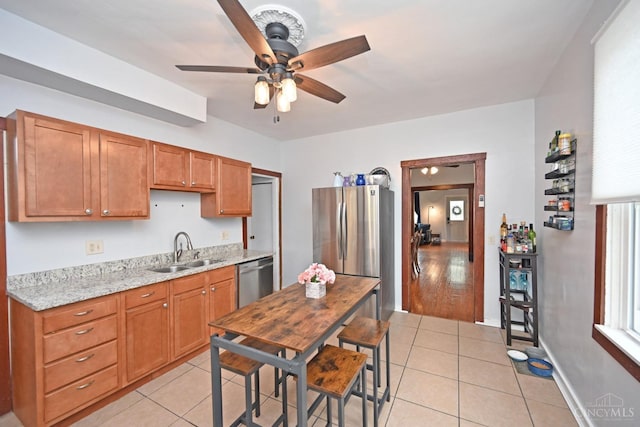 kitchen featuring brown cabinets, stainless steel appliances, a ceiling fan, light tile patterned floors, and a sink