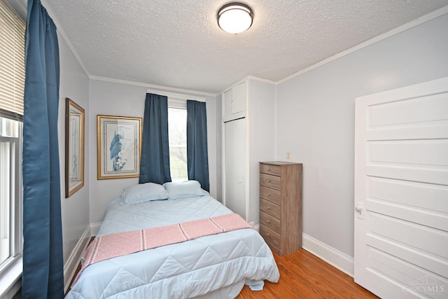 bedroom featuring baseboards, crown molding, wood finished floors, and a textured ceiling