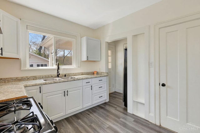 kitchen with a sink, light wood-style floors, gas range, light countertops, and white cabinetry