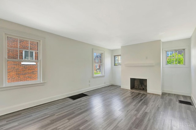 unfurnished living room with a fireplace with flush hearth, baseboards, wood finished floors, and visible vents