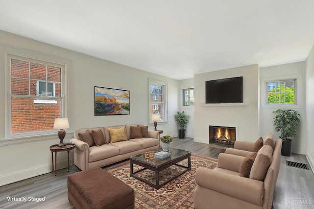 living area featuring visible vents, a glass covered fireplace, baseboards, and wood finished floors