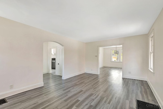 unfurnished room featuring visible vents, baseboards, wood finished floors, and arched walkways