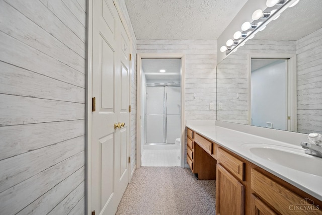 bathroom with a textured ceiling, wood walls, an enclosed shower, and vanity