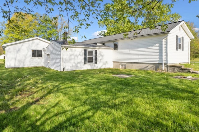 rear view of house featuring a lawn, a chimney, and metal roof