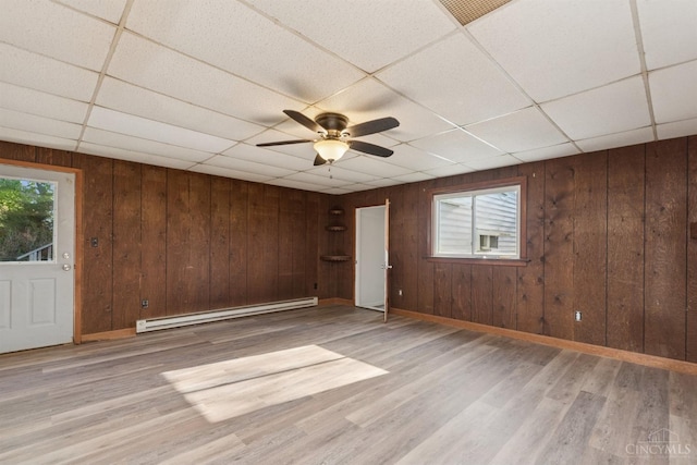 empty room with a baseboard heating unit, a paneled ceiling, ceiling fan, and a healthy amount of sunlight