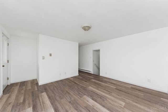 empty room with wood finished floors, baseboard heating, and baseboards