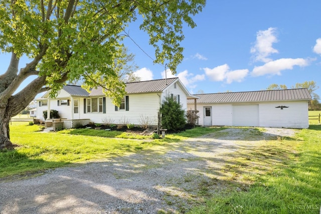 view of side of property with an outdoor structure, a yard, metal roof, a garage, and driveway