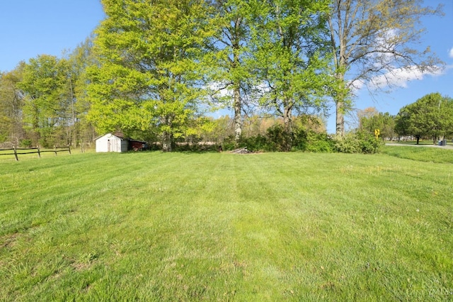 view of yard with fence, a rural view, an outdoor structure, and a storage unit