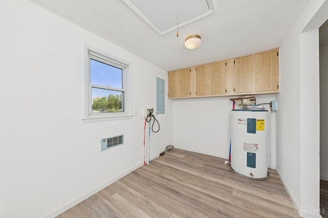 laundry room featuring attic access, light wood finished floors, cabinet space, electric panel, and electric water heater