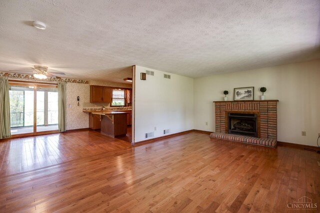 6139 N State Route 48, Clearcreek Twp, OH 45036 - unfurnished living room featuring a textured ceiling, light wood finished floors, healthy amount of natural light, a brick fireplace, and baseboards