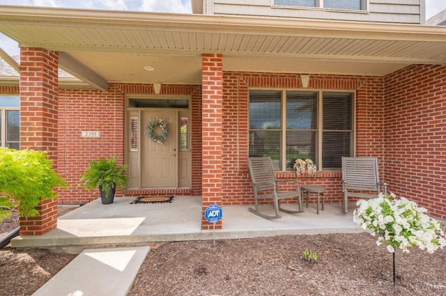entrance to property featuring a porch and brick siding