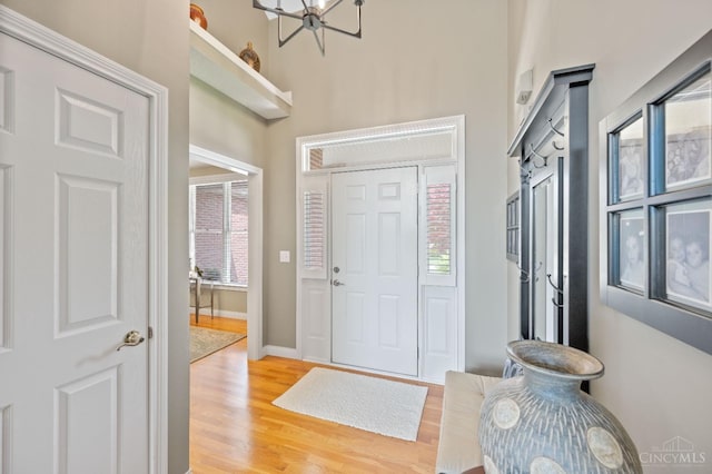 entrance foyer with baseboards, a high ceiling, light wood-type flooring, and a chandelier