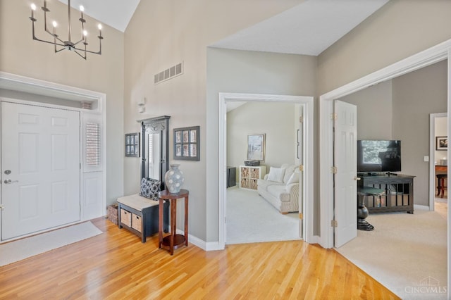 entryway featuring high vaulted ceiling, a chandelier, baseboards, wood finished floors, and visible vents