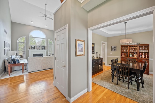 dining space with a fireplace, light wood-style flooring, a ceiling fan, baseboards, and visible vents