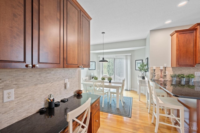 kitchen with light wood-style floors, recessed lighting, dark stone counters, brown cabinets, and backsplash