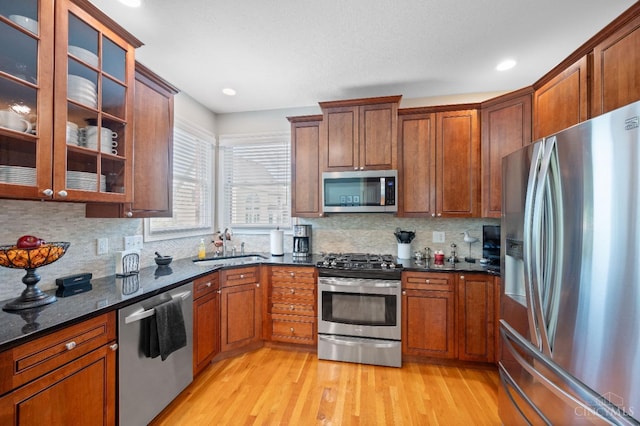 kitchen with a sink, decorative backsplash, stainless steel appliances, and light wood finished floors