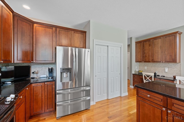 kitchen featuring dark stone counters, brown cabinets, tasteful backsplash, light wood-style flooring, and stainless steel appliances