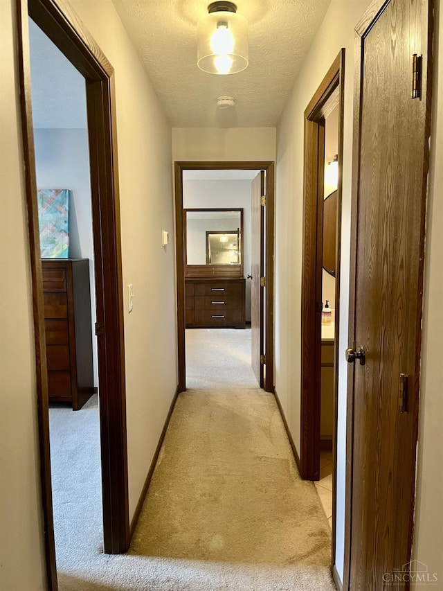 hall featuring light carpet, baseboards, and a textured ceiling