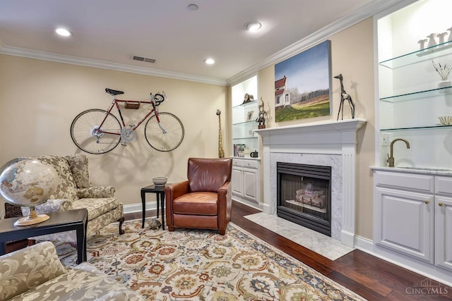 sitting room with wood finished floors, ornamental molding, a premium fireplace, baseboards, and built in features