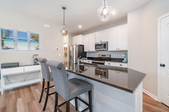 kitchen featuring a sink, stainless steel appliances, a breakfast bar, white cabinetry, and light wood-style floors