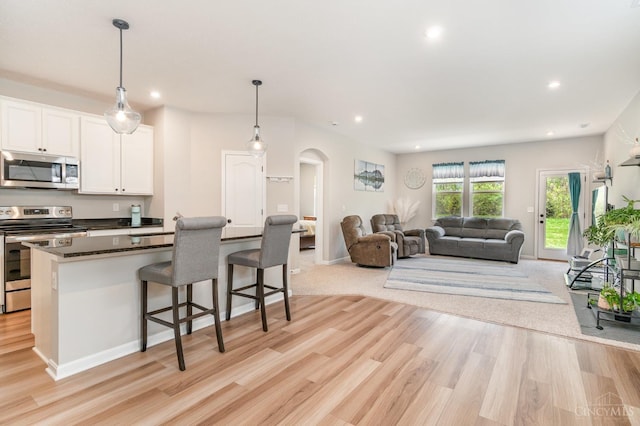 kitchen with light wood-style flooring, open floor plan, arched walkways, dark countertops, and appliances with stainless steel finishes