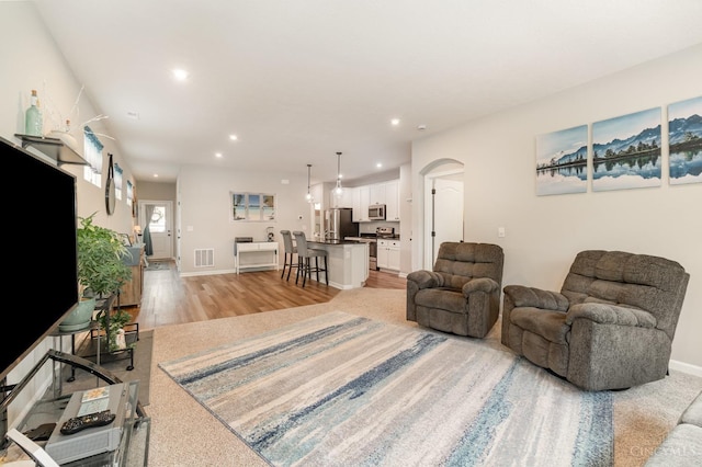 living area featuring arched walkways, light wood-type flooring, visible vents, and recessed lighting