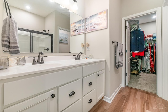 full bathroom featuring a sink, double vanity, a shower stall, and wood finished floors
