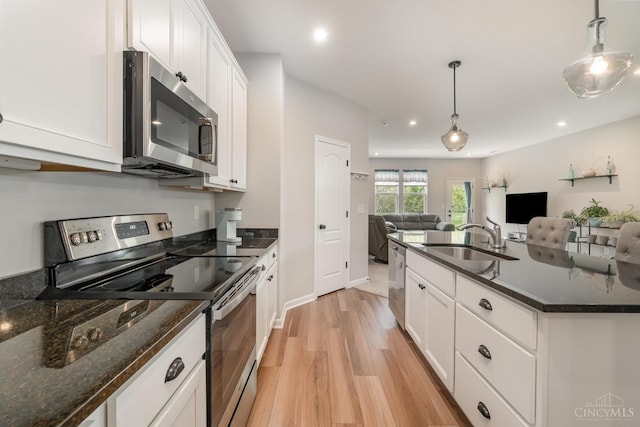 kitchen with light wood finished floors, a sink, stainless steel appliances, open floor plan, and white cabinets
