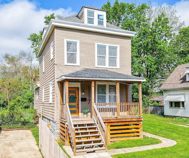 traditional style home featuring covered porch, stairway, fence, and a front lawn