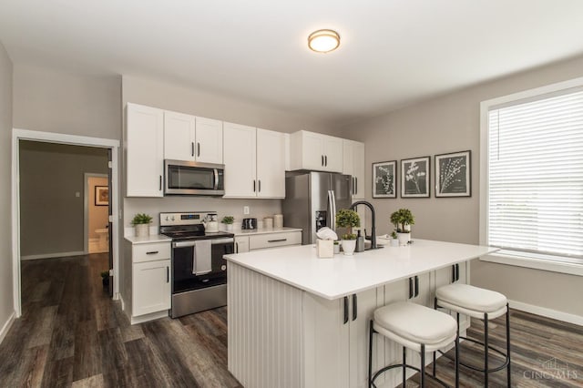 kitchen featuring stainless steel appliances, a kitchen breakfast bar, dark wood-style flooring, white cabinetry, and light countertops