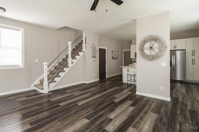 unfurnished living room with baseboards, stairway, ceiling fan, and dark wood-type flooring