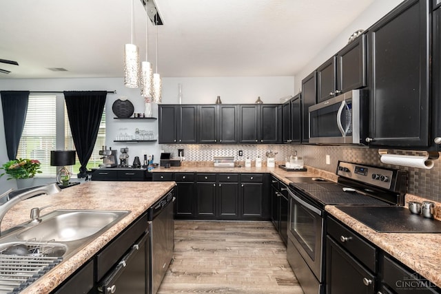 kitchen featuring stainless steel appliances, light wood-type flooring, dark cabinets, decorative light fixtures, and a sink