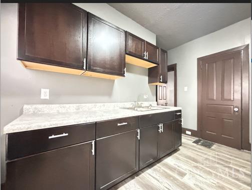 1239 Sliker Ave, Cincinnati, OH 45205 - kitchen with light wood finished floors, light countertops, a sink, and dark brown cabinetry
