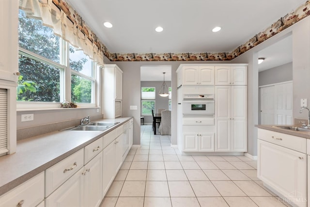 kitchen with a sink, white appliances, white cabinets, light countertops, and recessed lighting