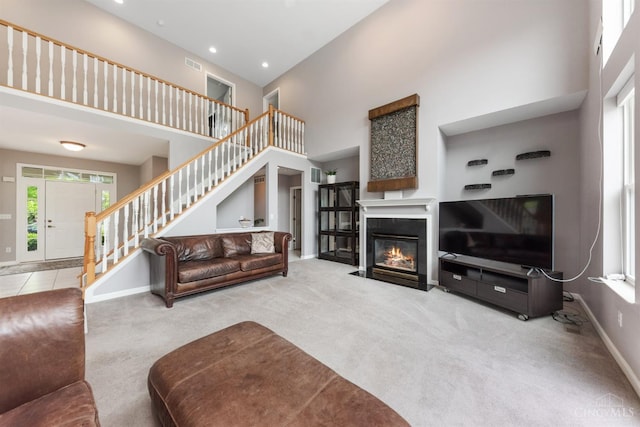 carpeted living area with a towering ceiling, baseboards, stairway, a fireplace with flush hearth, and recessed lighting