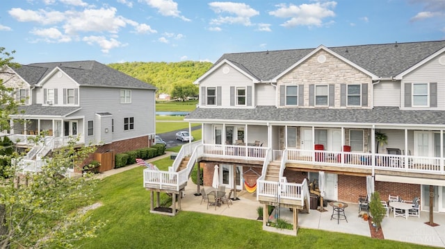 back of property featuring stairs, a lawn, a patio, a water view, and roof with shingles