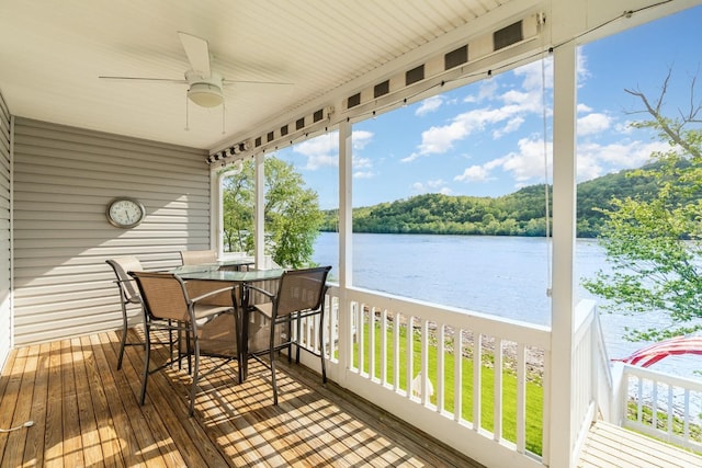 wooden deck with a water view, ceiling fan, outdoor dining space, and a wooded view