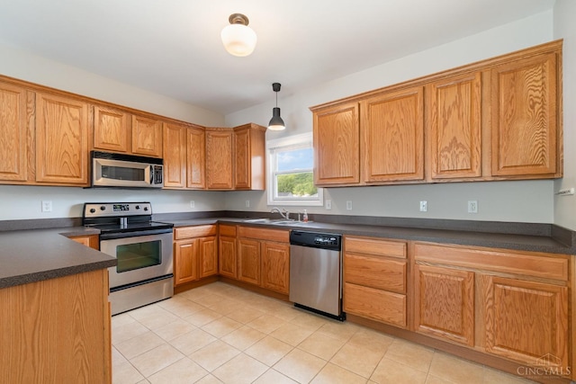 kitchen with stainless steel appliances, dark countertops, a sink, light tile patterned floors, and hanging light fixtures