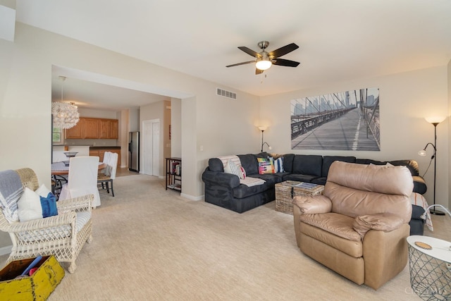 living room featuring ceiling fan, light colored carpet, baseboards, and a chandelier