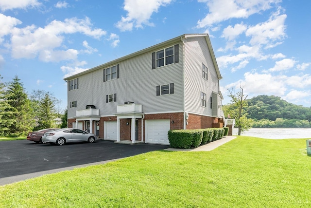 view of property with brick siding, a front yard, a water view, an attached garage, and asphalt driveway