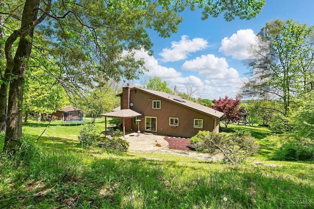 11675 New Biddinger Rd, Harrison Twp, OH 45030 - back of house with a trampoline, a patio, a chimney, and a lawn
