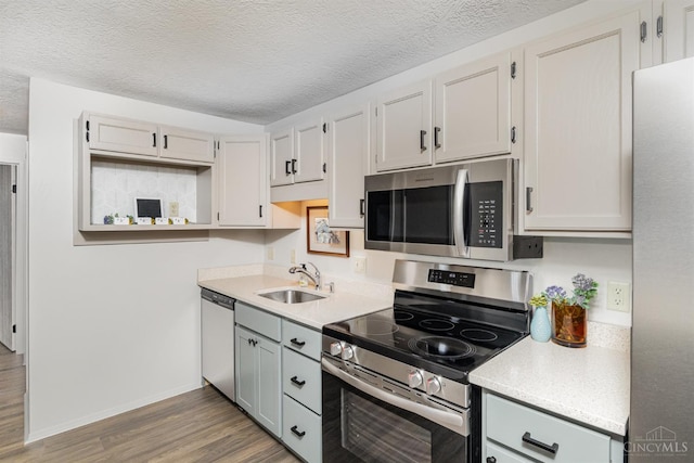 kitchen featuring stainless steel appliances, a sink, wood finished floors, light countertops, and baseboards