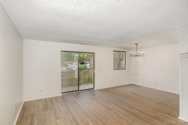 spare room featuring a chandelier, wood finished floors, a textured ceiling, and baseboards