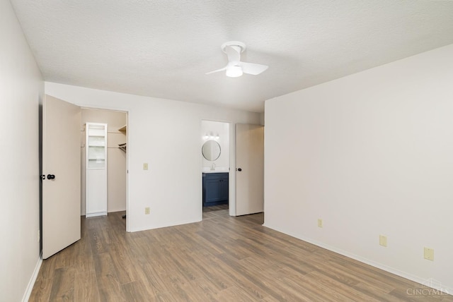 unfurnished bedroom with wood finished floors, a walk in closet, a closet, ceiling fan, and connected bathroom