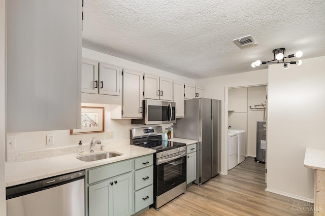 kitchen featuring stainless steel appliances, a sink, washer and dryer, water heater, and light wood-type flooring