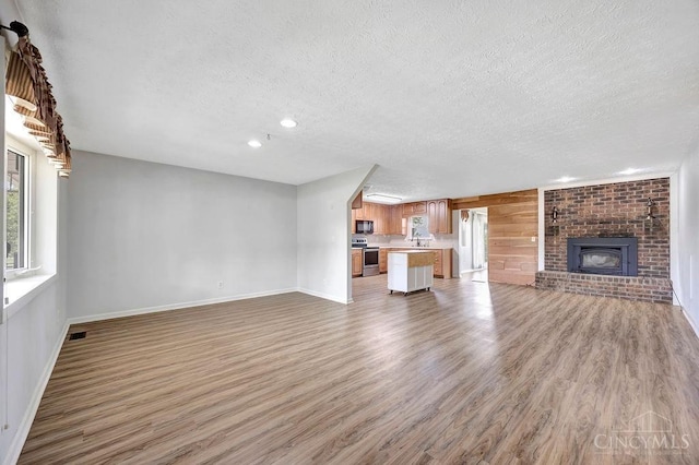2774 N Law Rd, Reily Twp, OH 45056 - unfurnished living room with a textured ceiling, light wood finished floors, baseboards, a brick fireplace, and recessed lighting