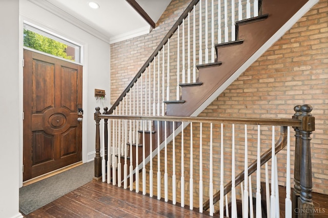foyer with brick wall, wood-type flooring, crown molding, stairway, and baseboards
