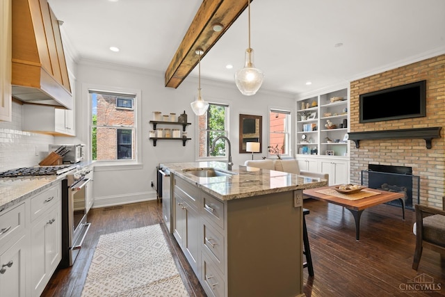 kitchen with appliances with stainless steel finishes, a sink, custom range hood, open floor plan, and ornamental molding