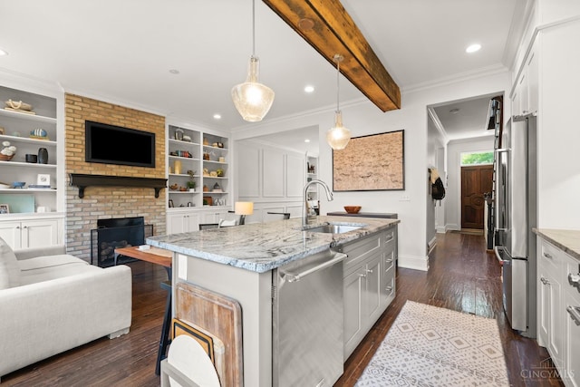 kitchen with appliances with stainless steel finishes, a sink, open floor plan, dark wood-style flooring, and light stone countertops