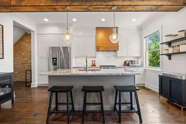 kitchen featuring high quality fridge, a sink, white cabinets, a kitchen island with sink, and a breakfast bar area